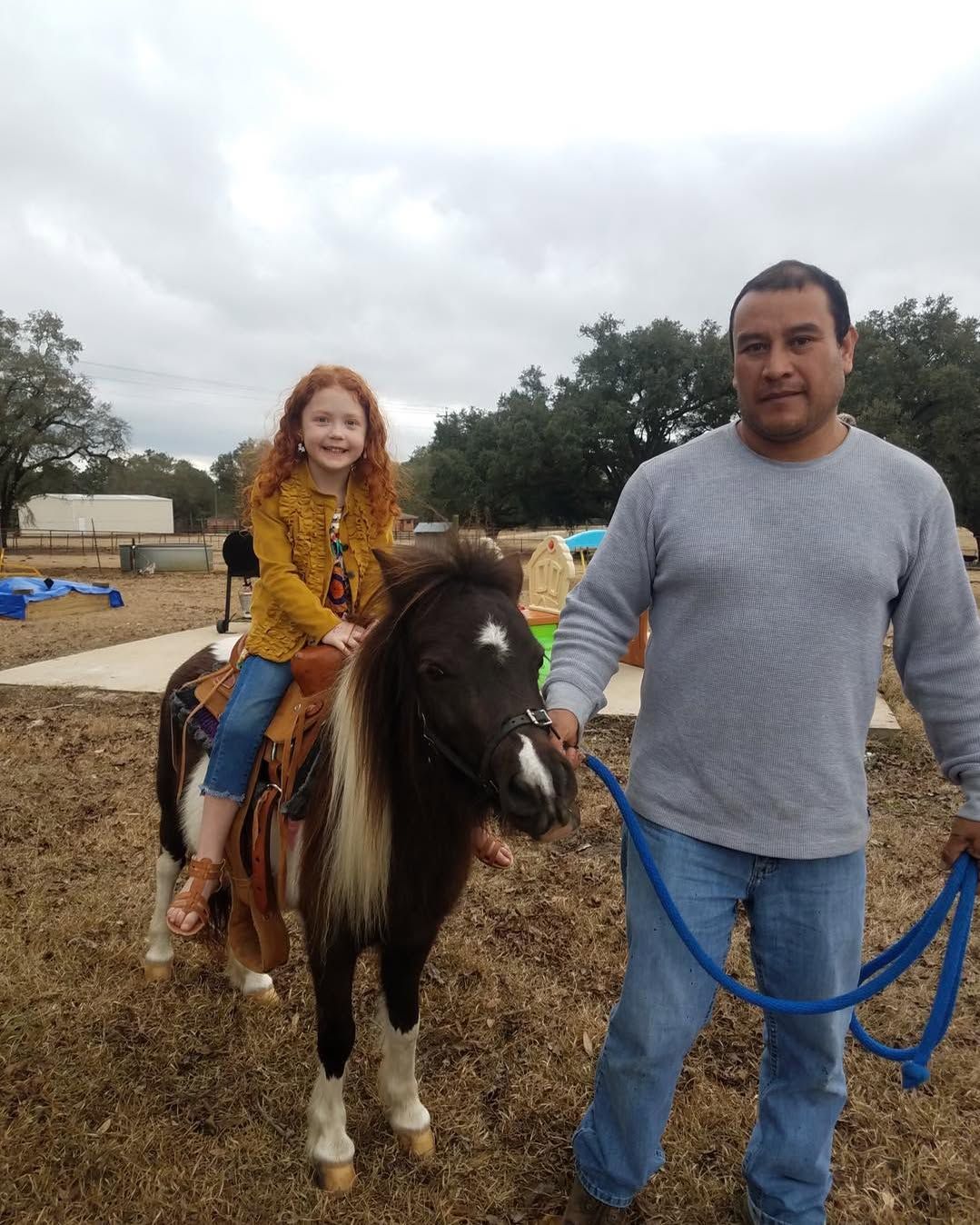 A little girl is riding a pony next to a man