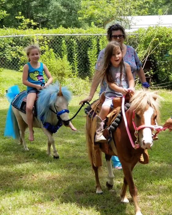 A woman and two little girls are riding ponies in the grass.