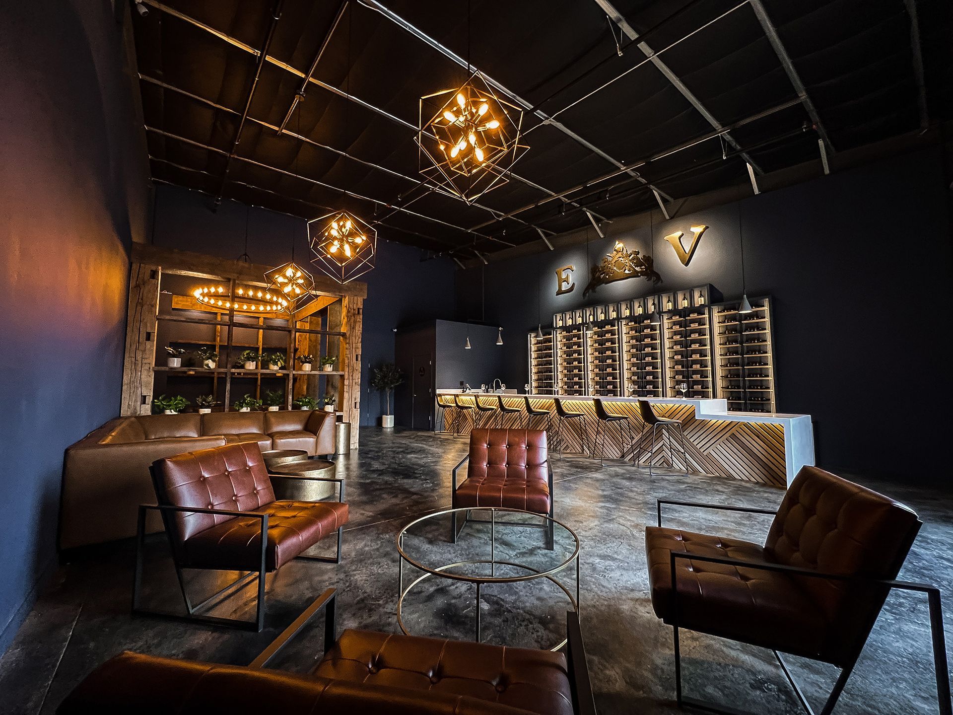 A dimly lit wine bar with leather chairs, wood shelving and a bar.