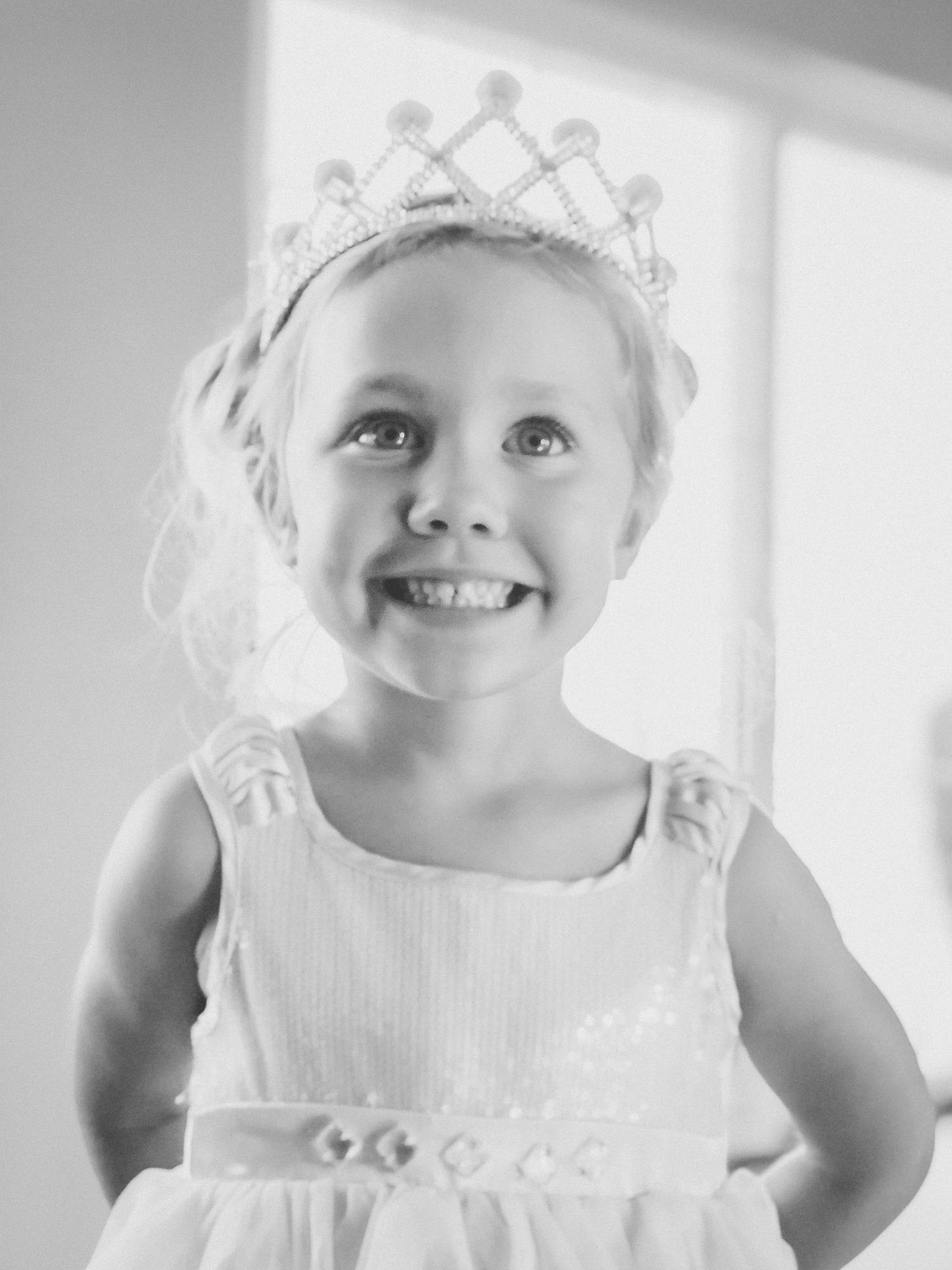 Girl wearing a tiara and dress, smiling, looking upwards.