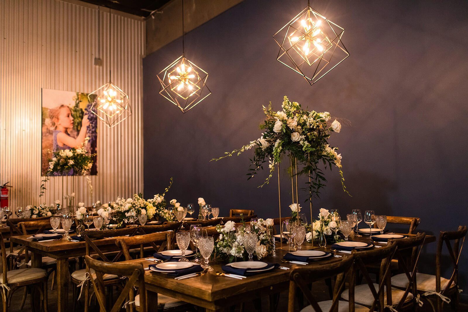 Wedding reception hall with tables set for dining, floral centerpieces, and decorative hanging lights.