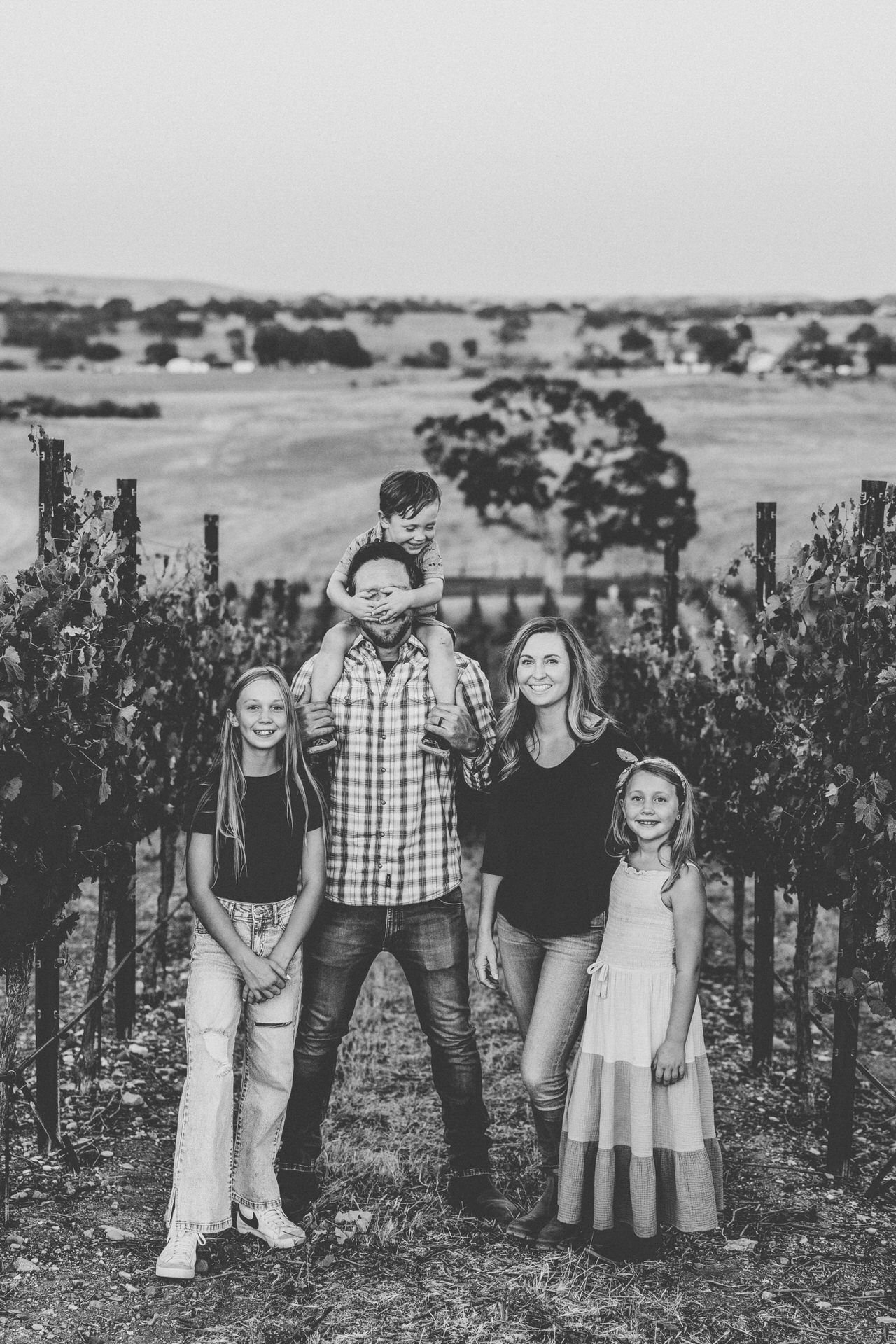 Family of five poses in a vineyard at sunset.