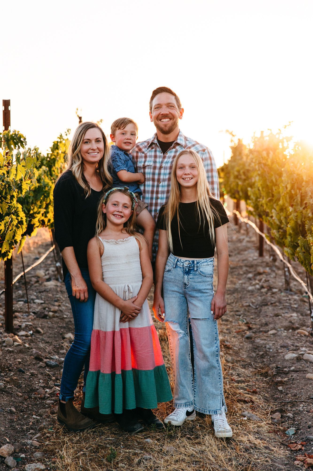 Family of five poses in a vineyard at sunset.