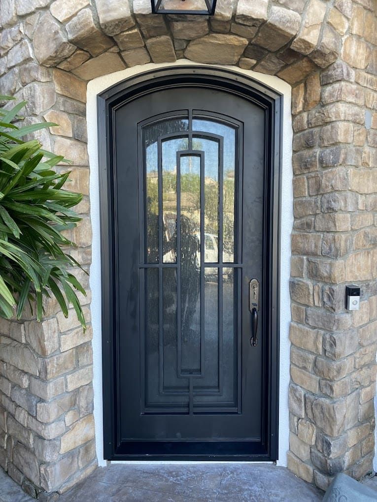 Black front door with decorative glass set in a stone archway, with a keypad on the right wall