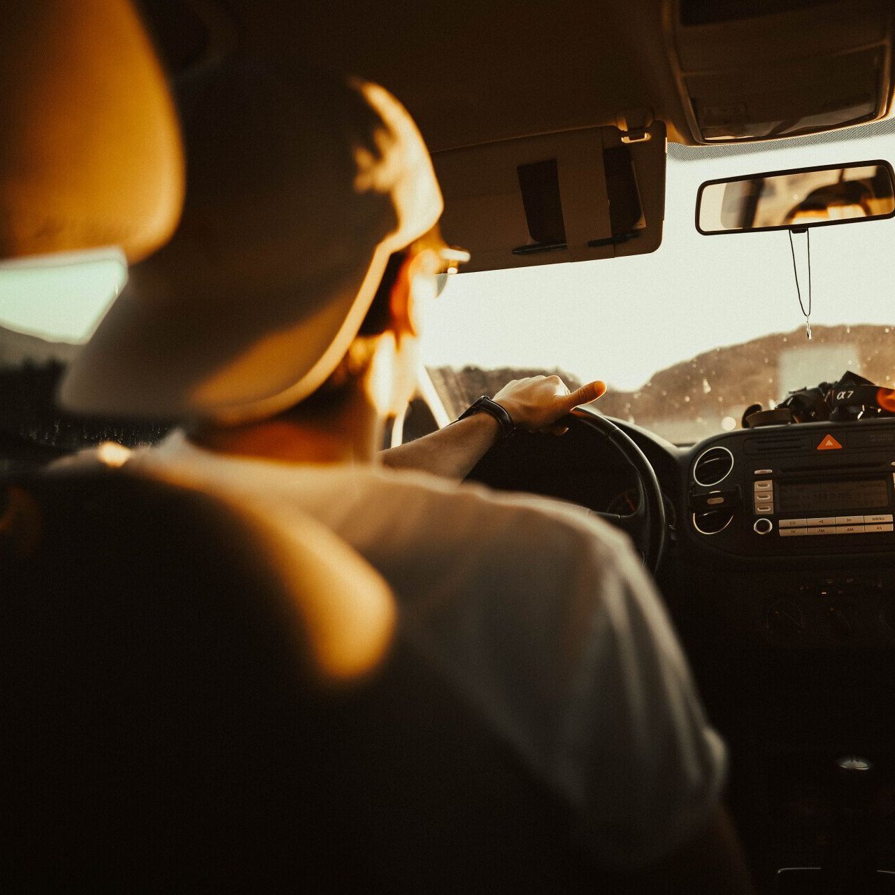 A man in a baseball cap is driving a car