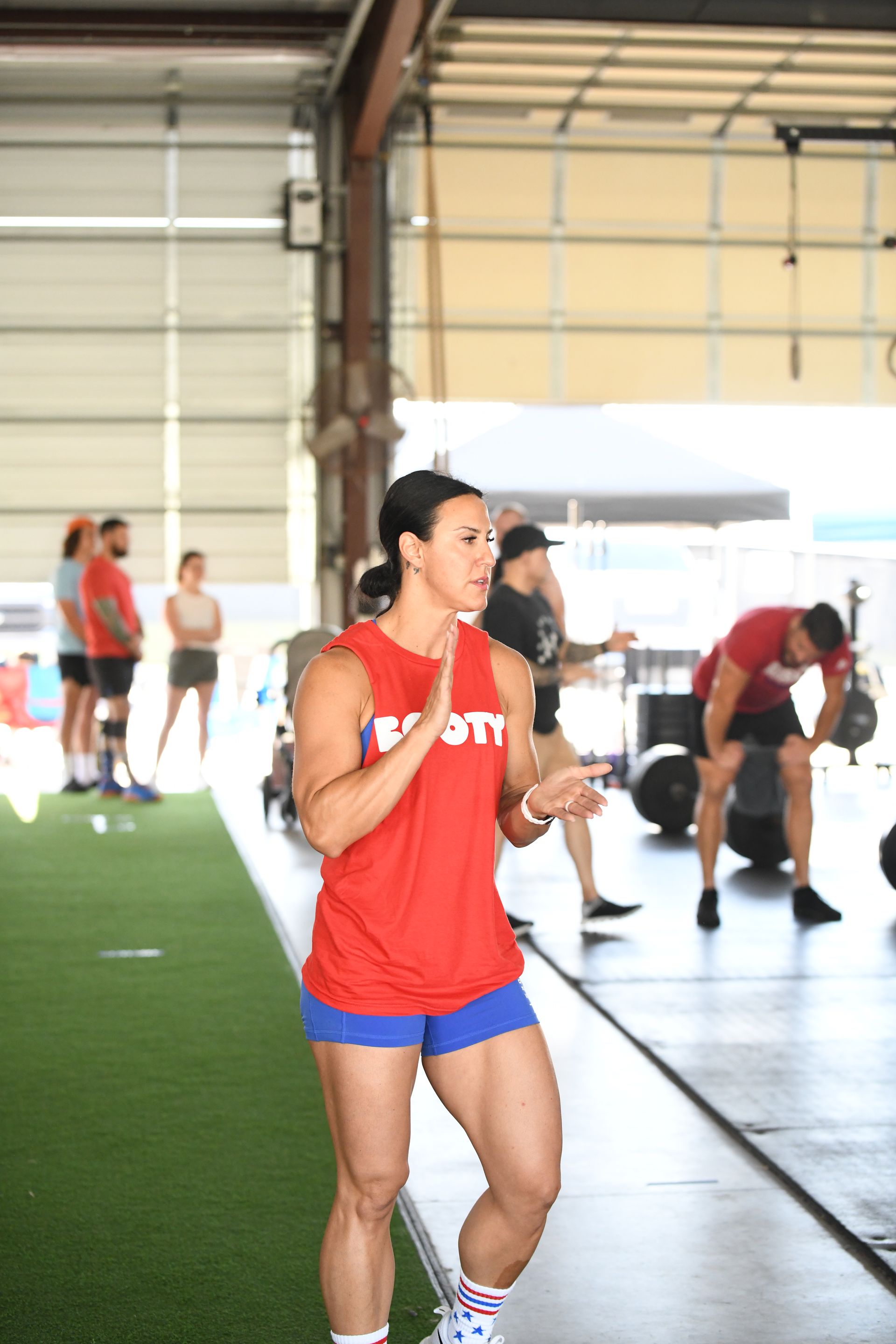 A woman in a red tank top and blue shorts is running in a gym.