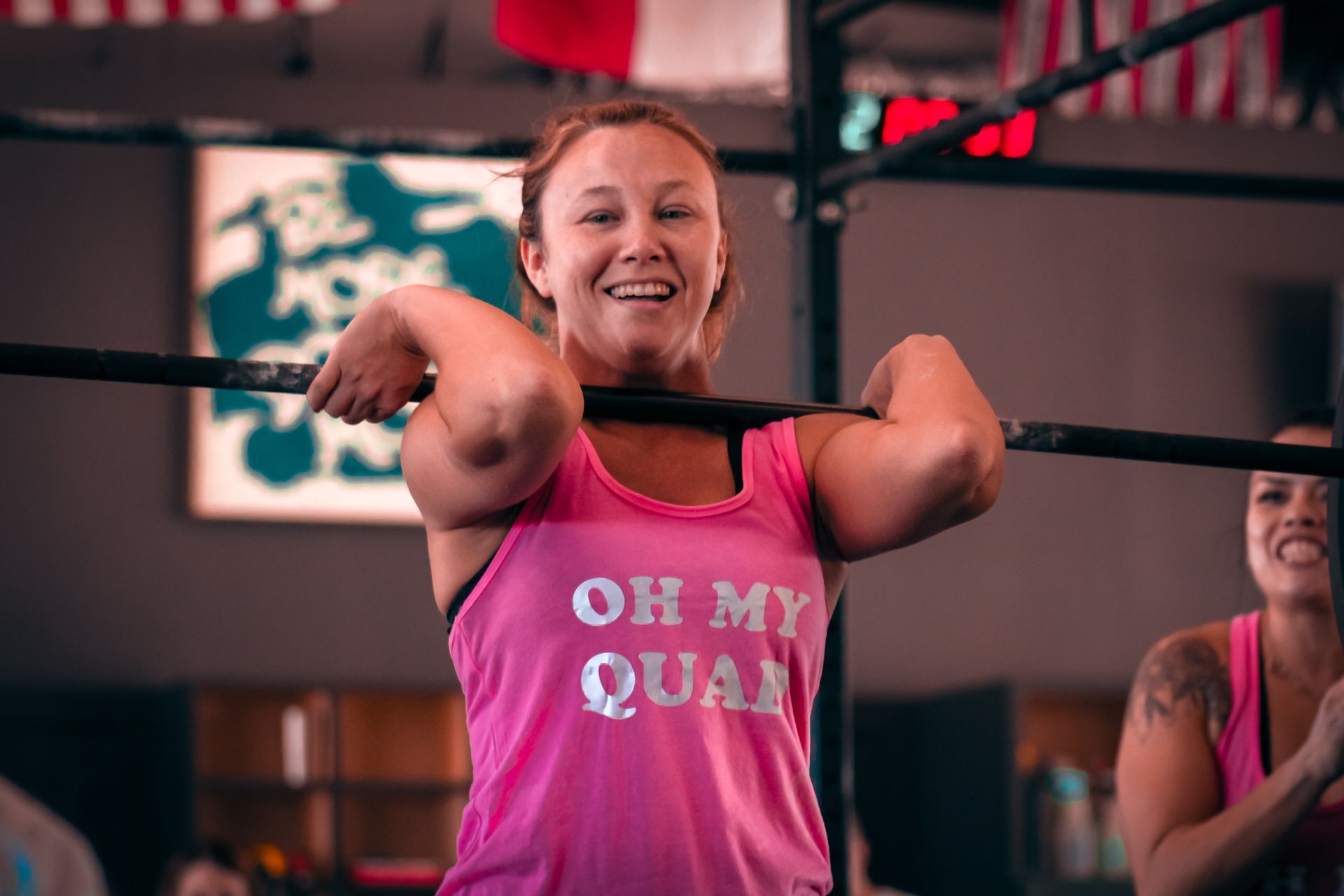 A woman in a pink tank top is lifting a barbell in a gym.
