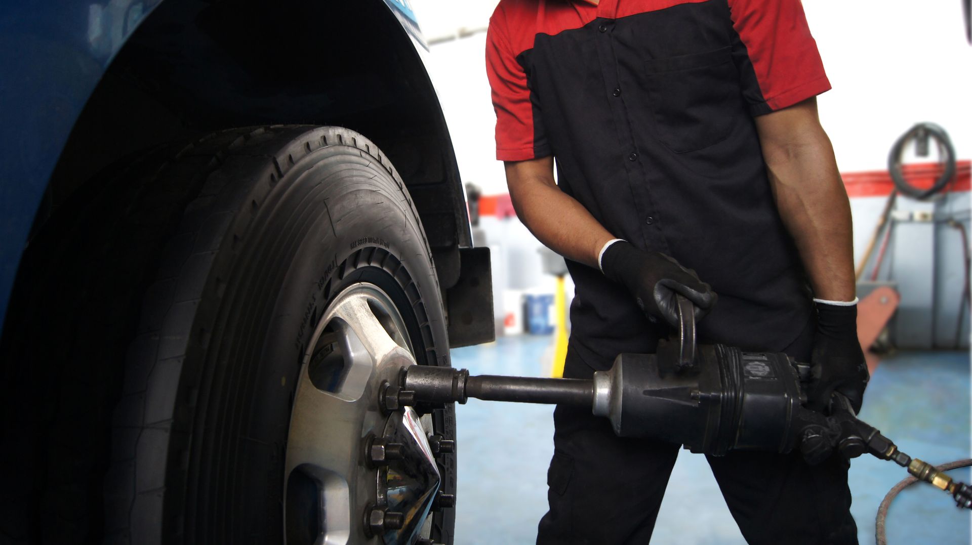 Mechanic using an impact wrench to remove a tire from a blue vehicle.