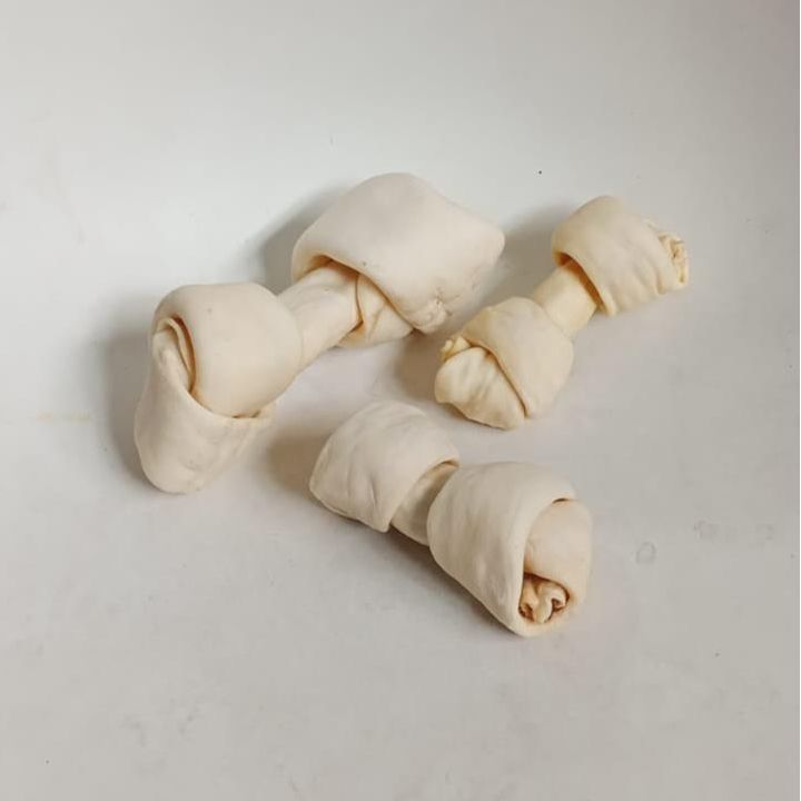 Tres masticables blancos para perros, anudados en el centro, sobre una superficie blanca.