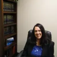 Woman in blazer smiles, seated in front of a bookshelf, likely in an office.