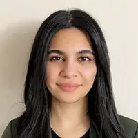 Woman with dark hair smiles, against a neutral background. She wears a dark top.