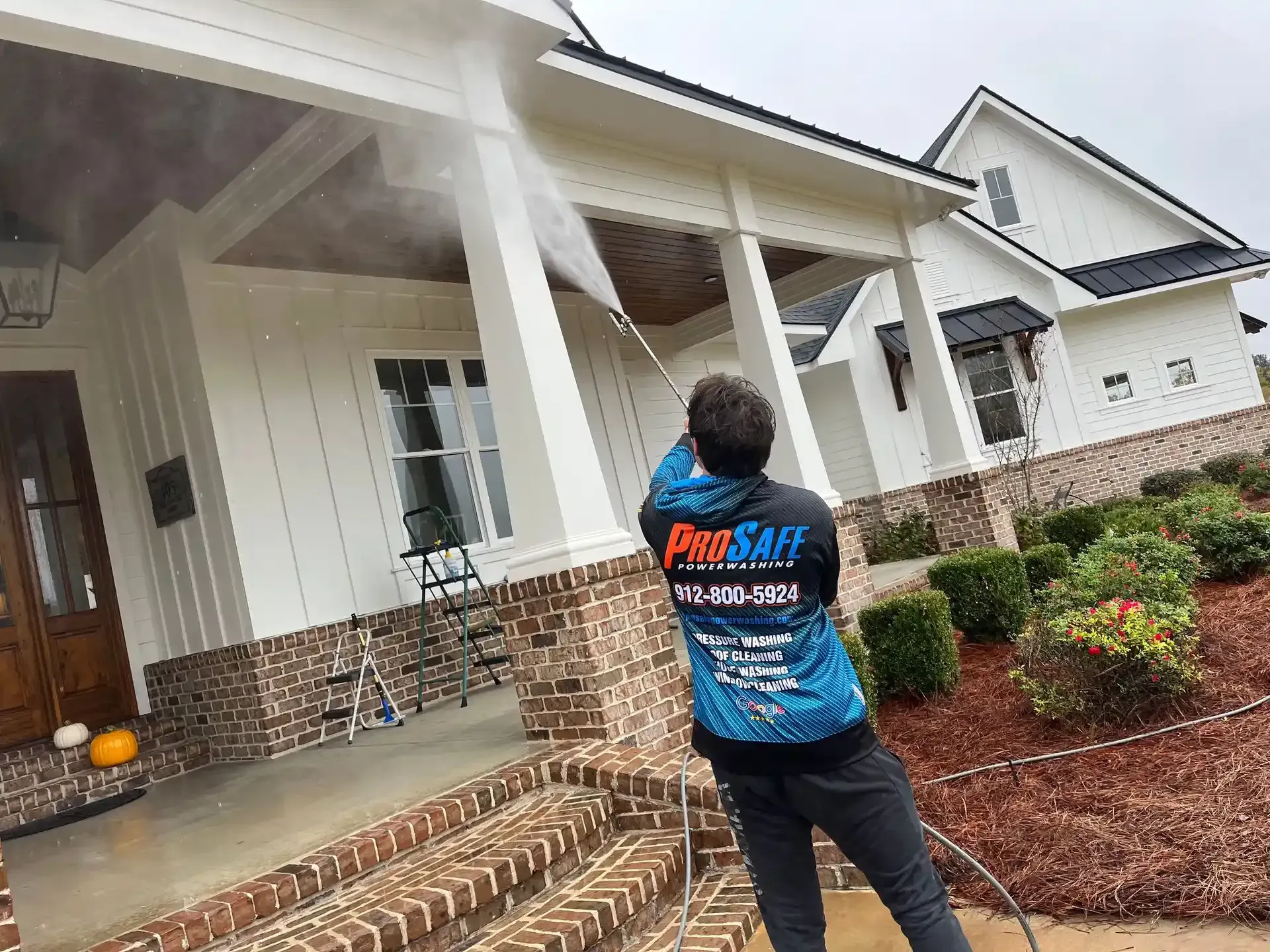 A man is cleaning the front of a house with a pressure washer.