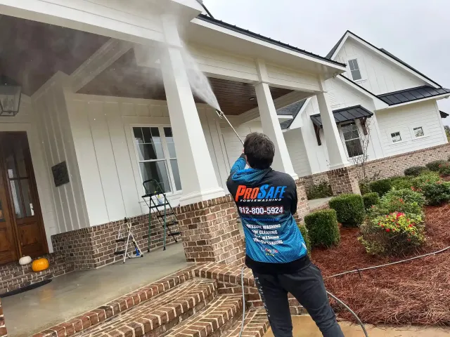 A man is cleaning the front of a house with a pressure washer.