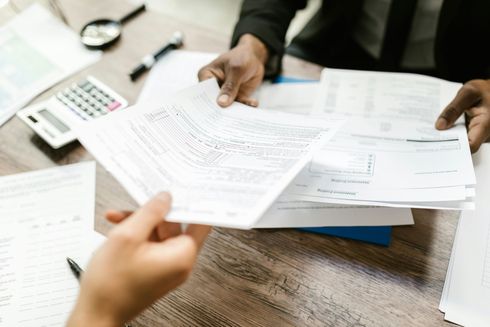 A man is holding a piece of paper over a pile of papers on a table.