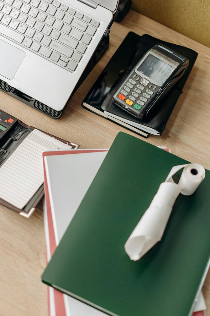 A desk with a laptop , calculator , notebooks , and a tie.