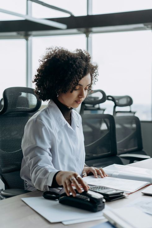 A woman in a lab coat is sitting at a desk using a calculator.