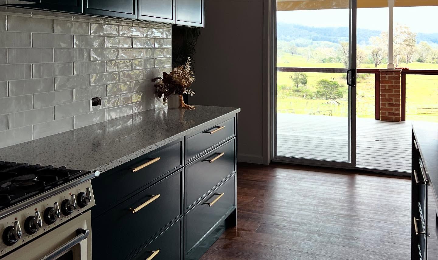 Kitchen with blue cabinets, white backsplash, and a view of a green landscape through sliding doors.— Onyx Detailed Joinery in Shellharbour, NSW