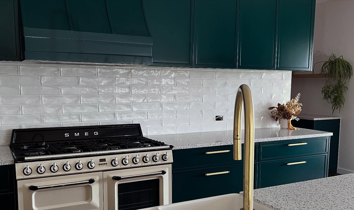 Emerald green kitchen with white backsplash, gold faucet, and off-white stove.— Onyx Detailed Joinery in Unanderra, NSW