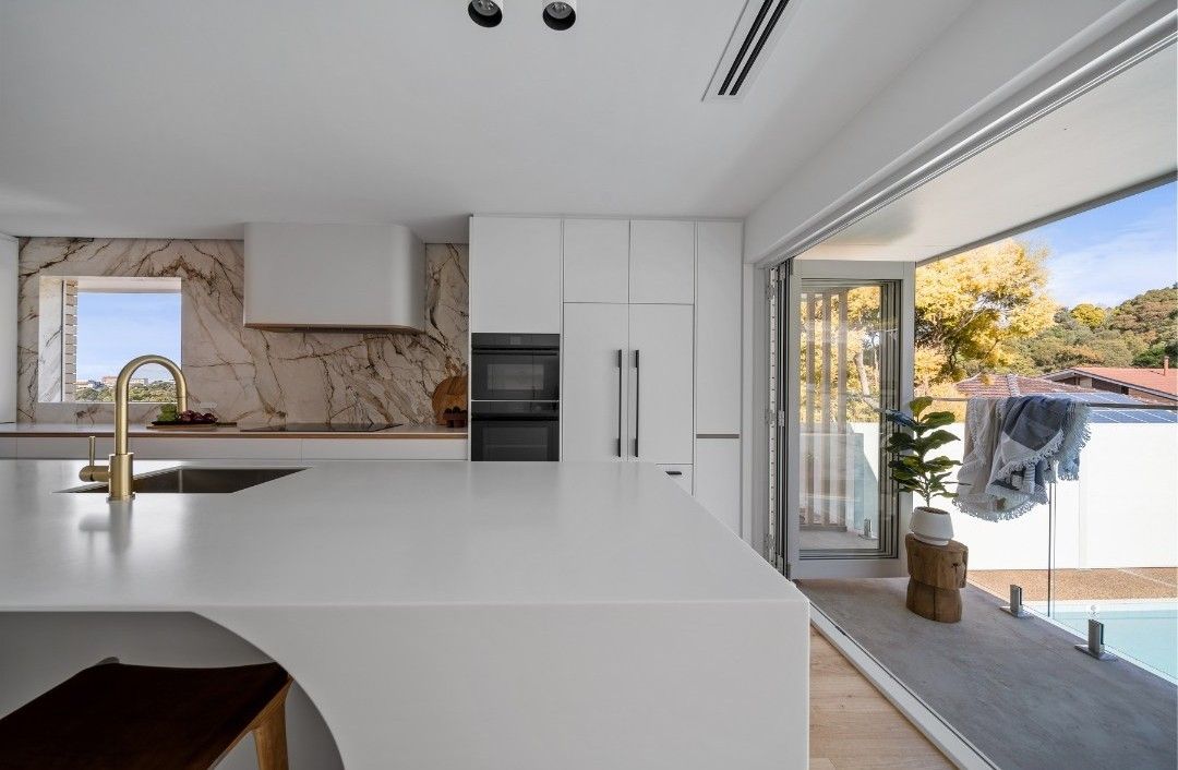 Modern white kitchen with marble backsplash, island, and open doors to a pool area. — Onyx Detailed Joinery in Unanderra, NSW