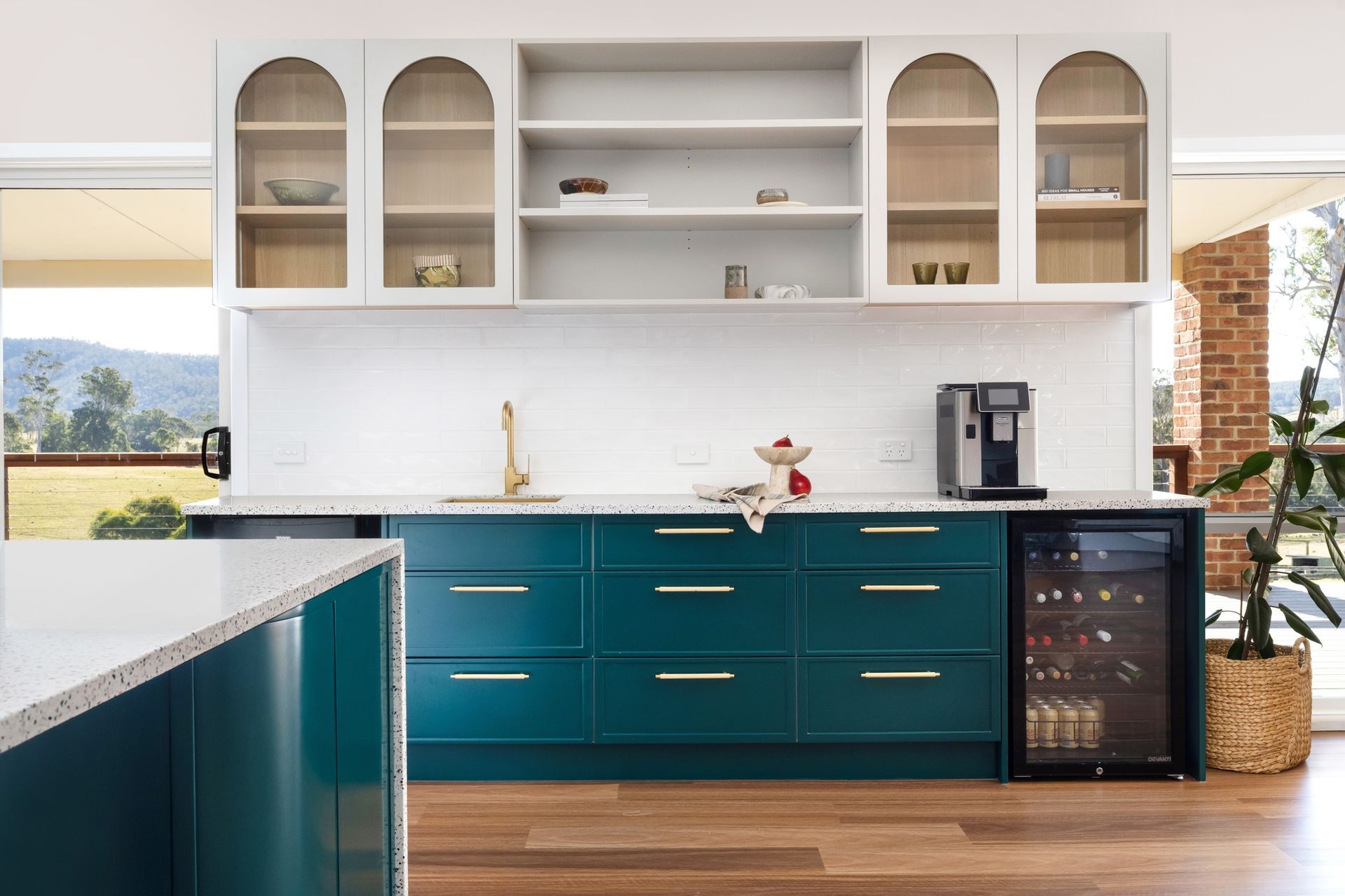 Teal kitchen with white cabinets, gold hardware, and a wine fridge.