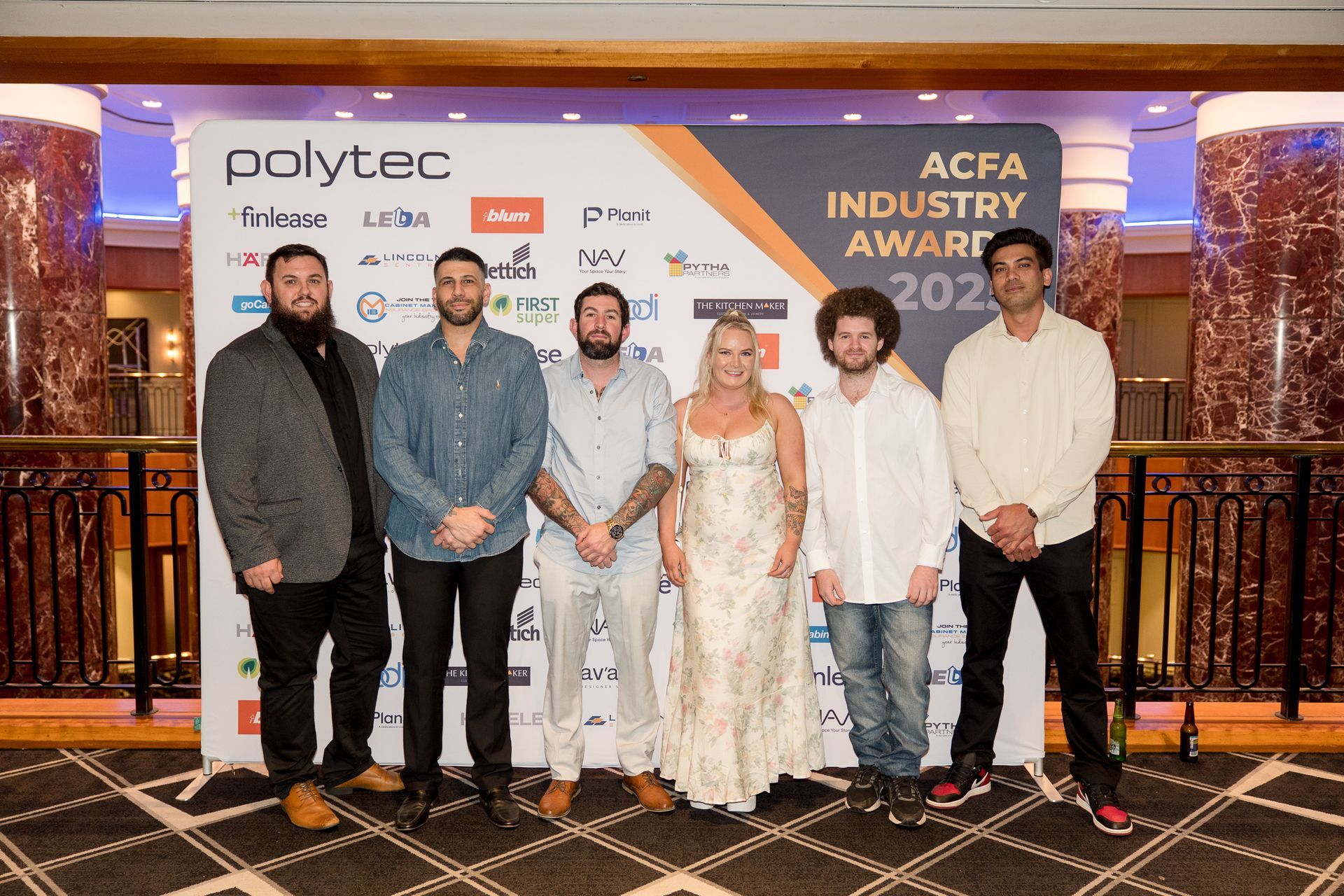 Group of six people posing in front of a backdrop with logos and 