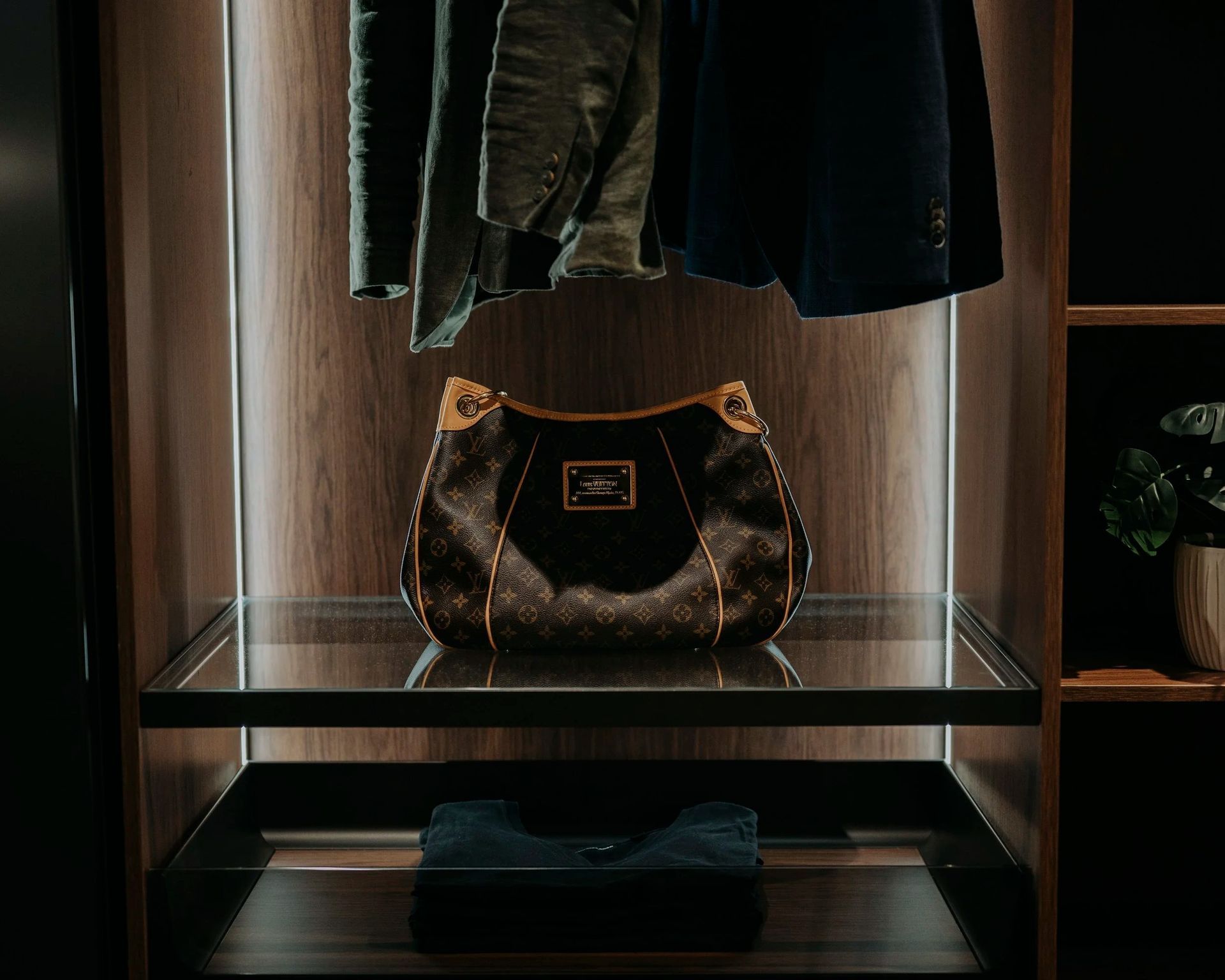 Handbag on a glass shelf in a closet with hanging jackets and a folded garment. — Onyx Detailed Joinery in Unanderra, NSW