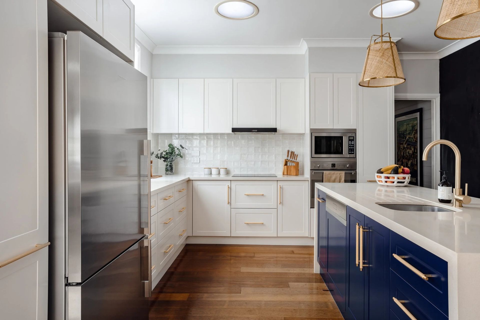 Modern kitchen with white and blue cabinets, stainless steel refrigerator, and wooden floors. — Onyx Detailed Joinery in Unanderra, NSW