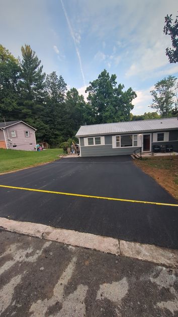 A house is sitting on top of a lush green field next to a paved driveway.