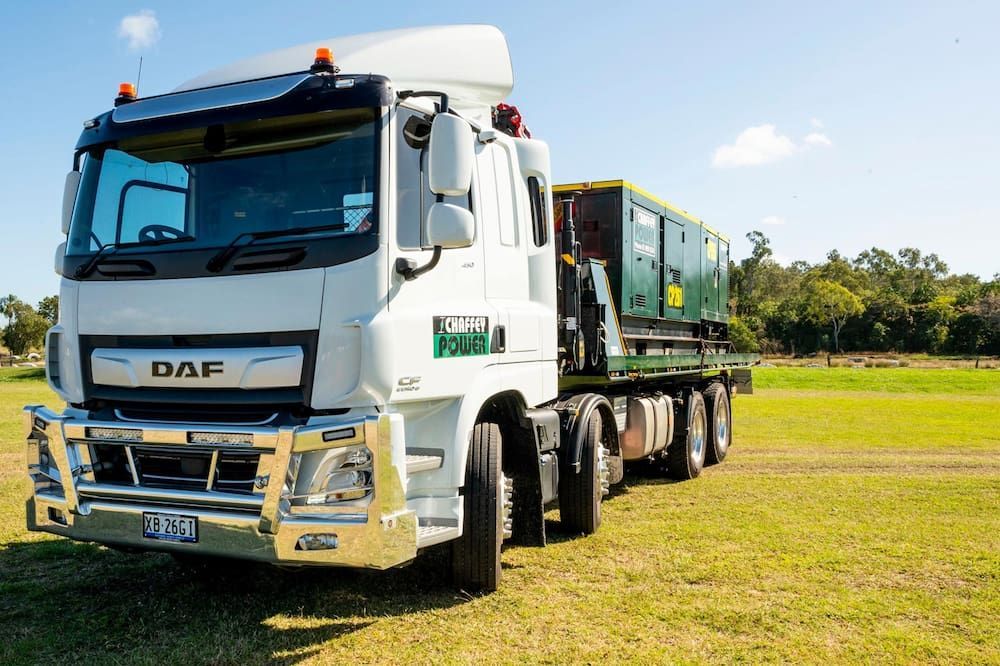 White truck transporting a generator on a flatbed in an open field.