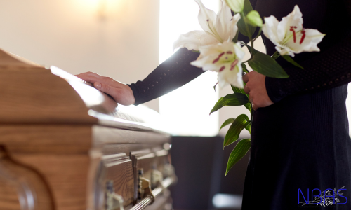 A woman is holding flowers in front of a coffin at a funeral.