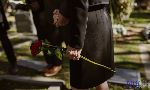 A woman is holding a red rose in her hand in a cemetery.