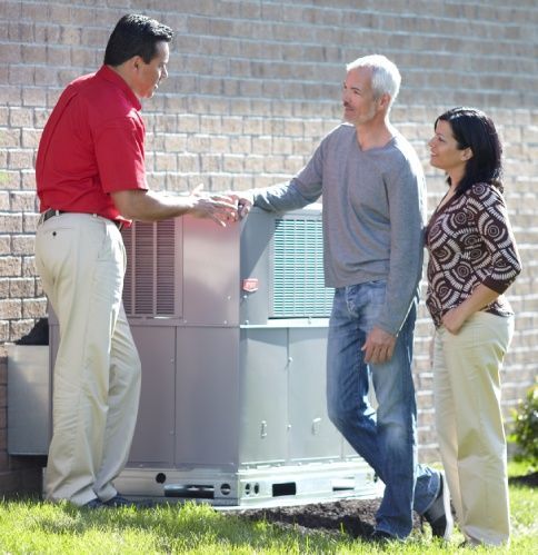 HVAC technician discussing with a couple next to an air conditioning unit outside a house.