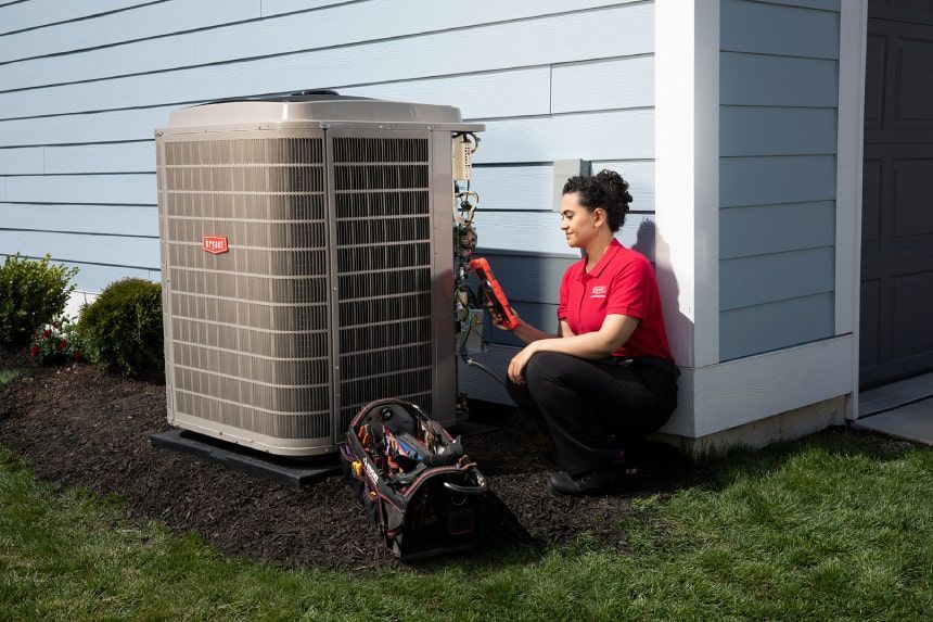 Woman in red shirt servicing an air conditioning unit outside a house.