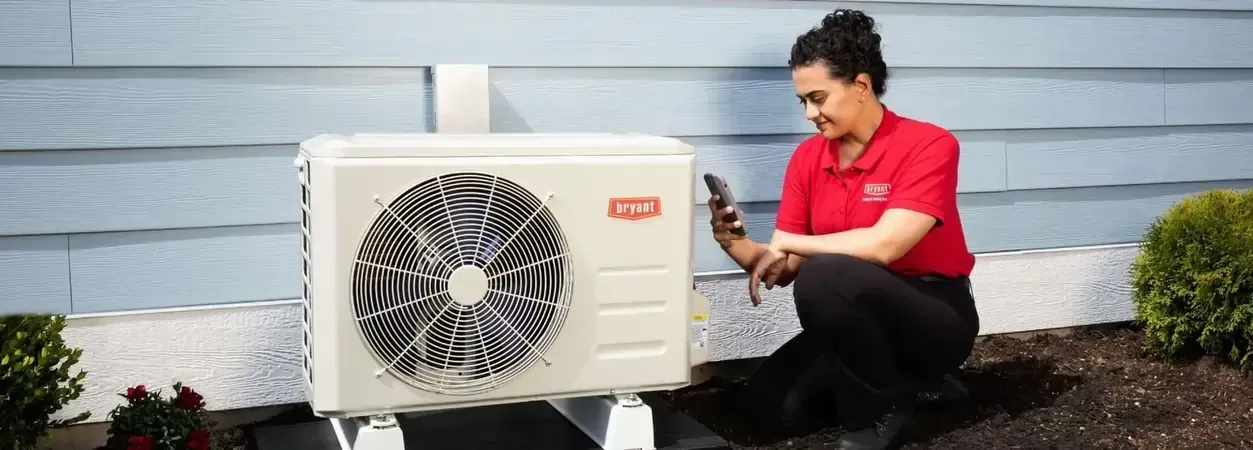 Woman in red shirt taking a photo of an AC unit outdoors.