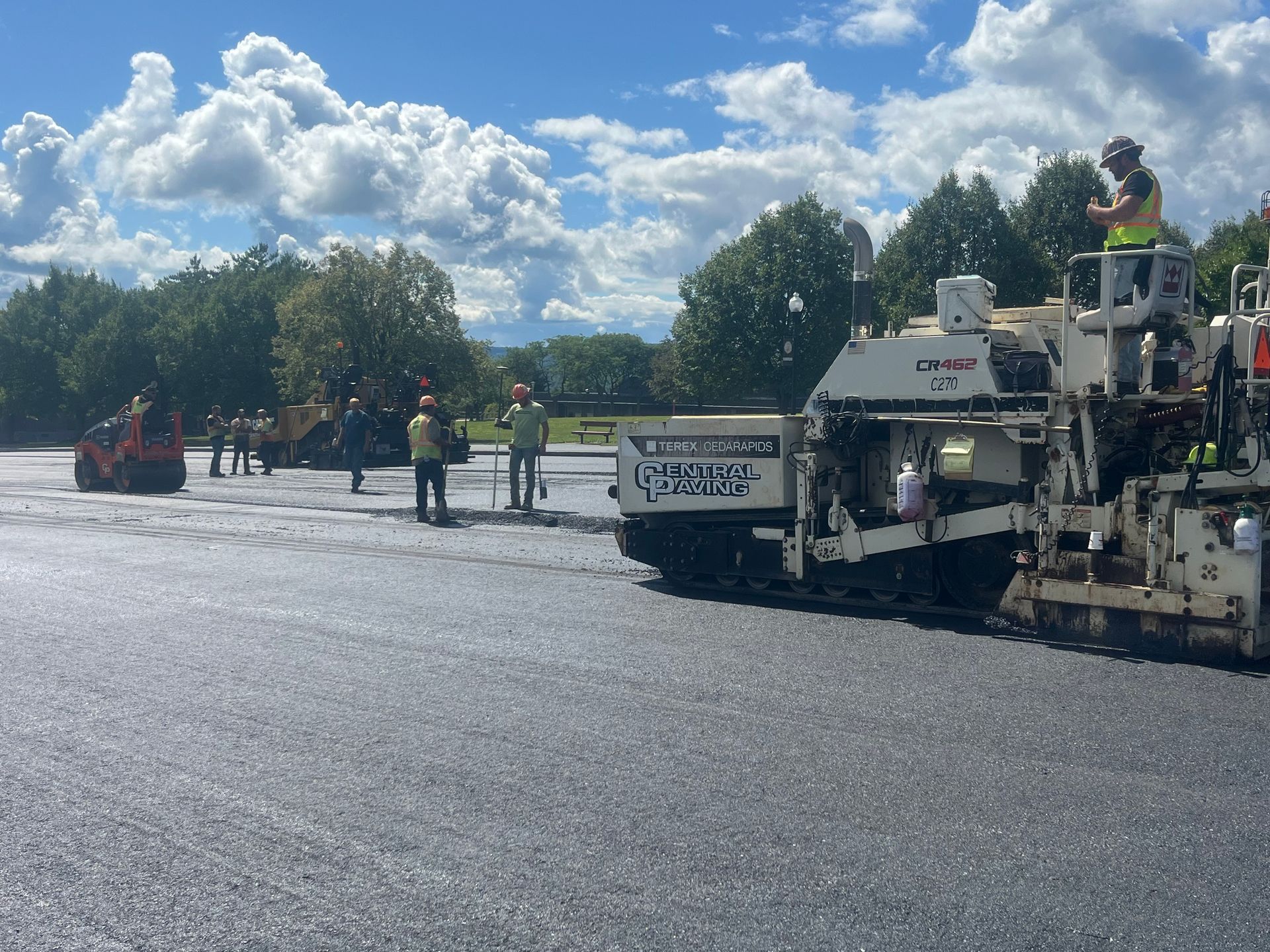 Road paving crew working on a wide road under a blue sky with clouds