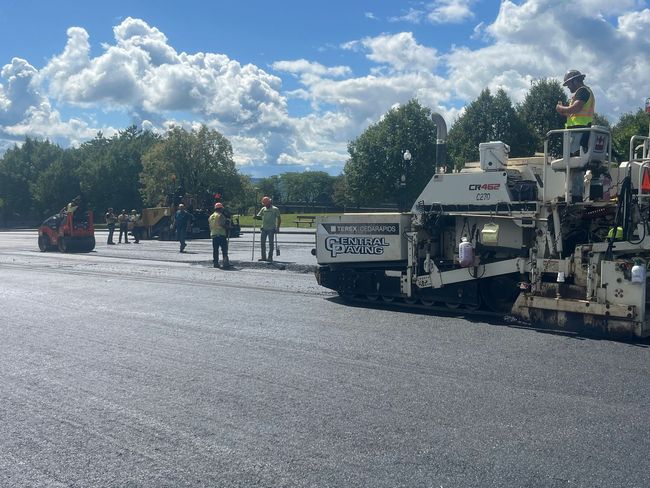 Workers use tools to spread and smooth hot asphalt during a road paving project.