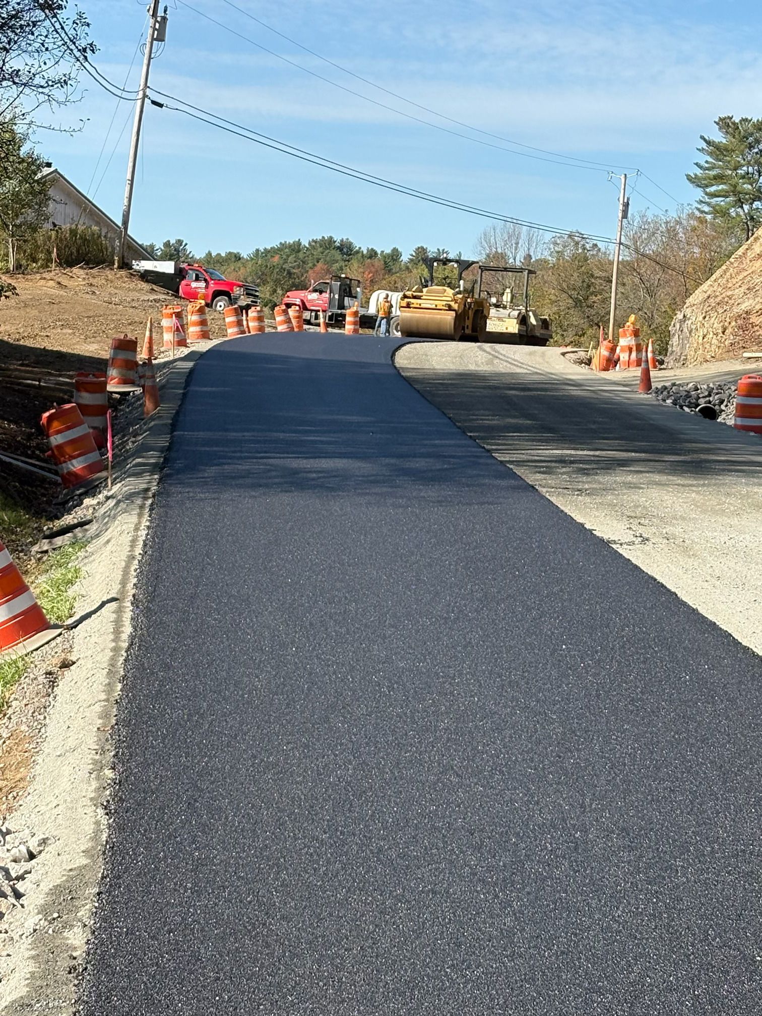 Freshly paved road with construction barriers and equipment on a sunny hillside road