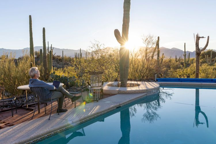 Person relaxing by a pool at sunset in a desert garden with cacti and mountains in the background