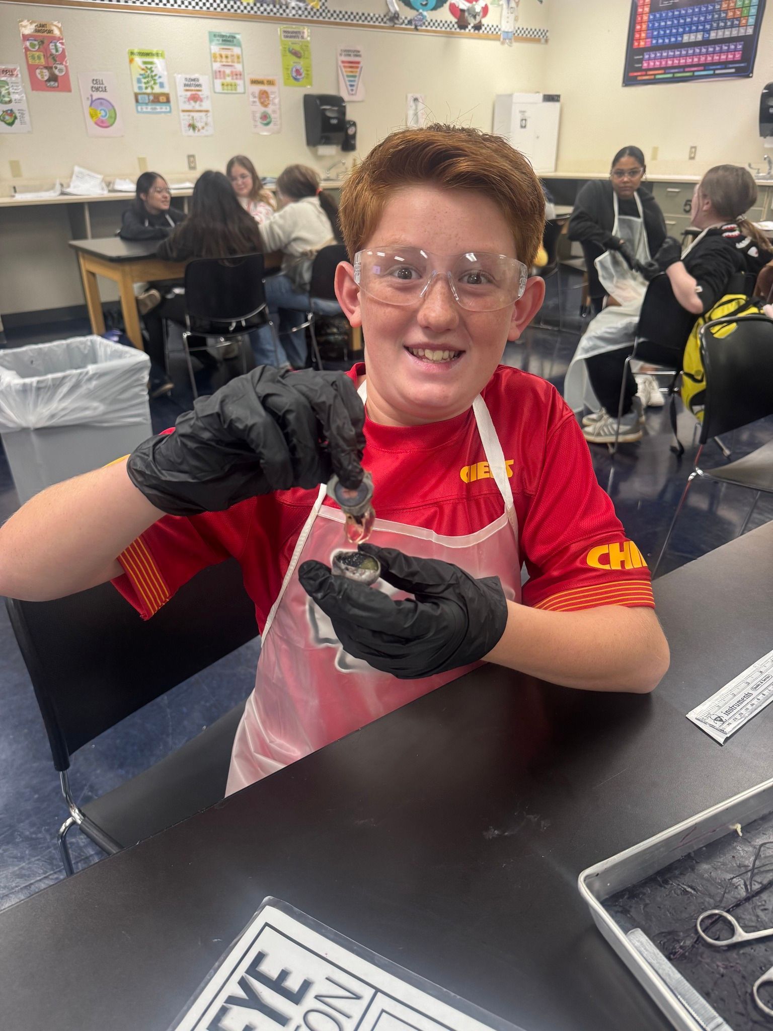 Boy in safety glasses and gloves dissecting an eye in a classroom.