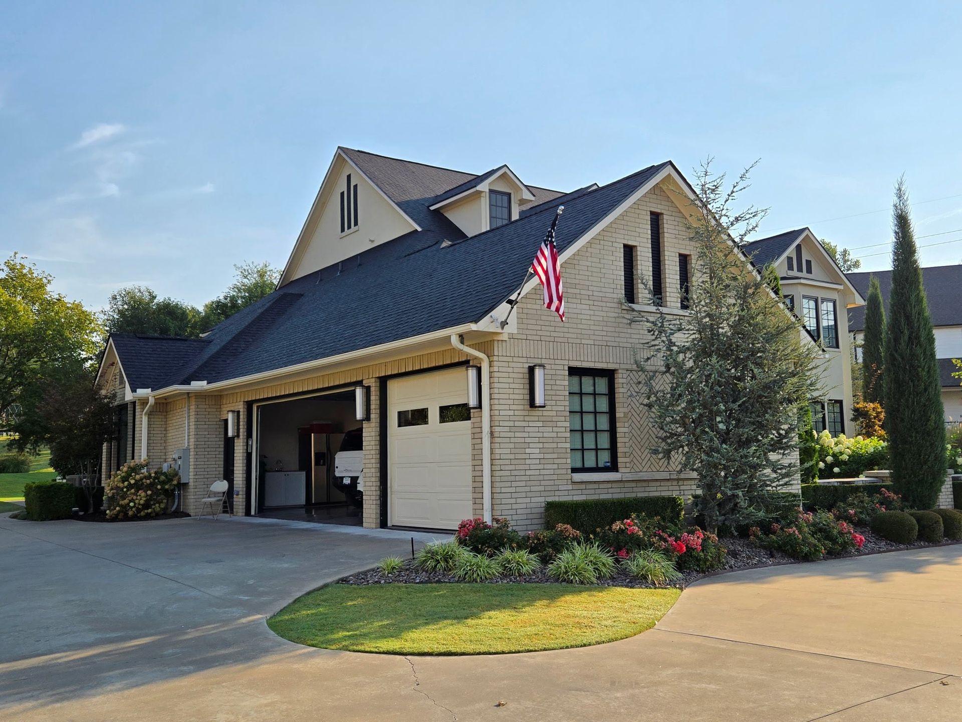 Beige house with open garage, American flag, and manicured landscaping.
