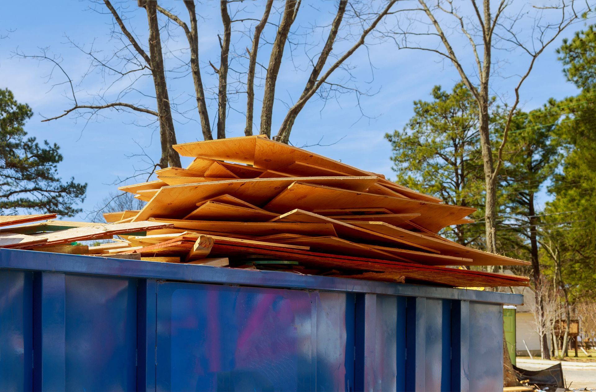 A blue dumpster filled with a pile of wood.