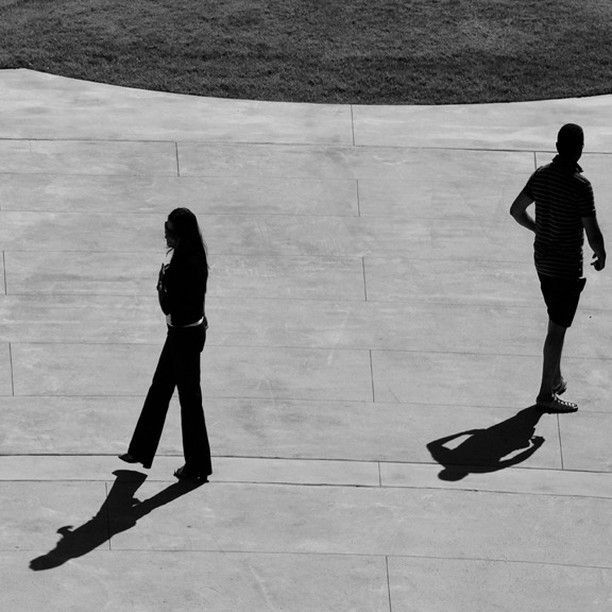 Two people walking on a sidewalk with their shadows on the ground