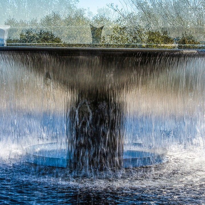 A fountain with water coming out of it and trees in the background.