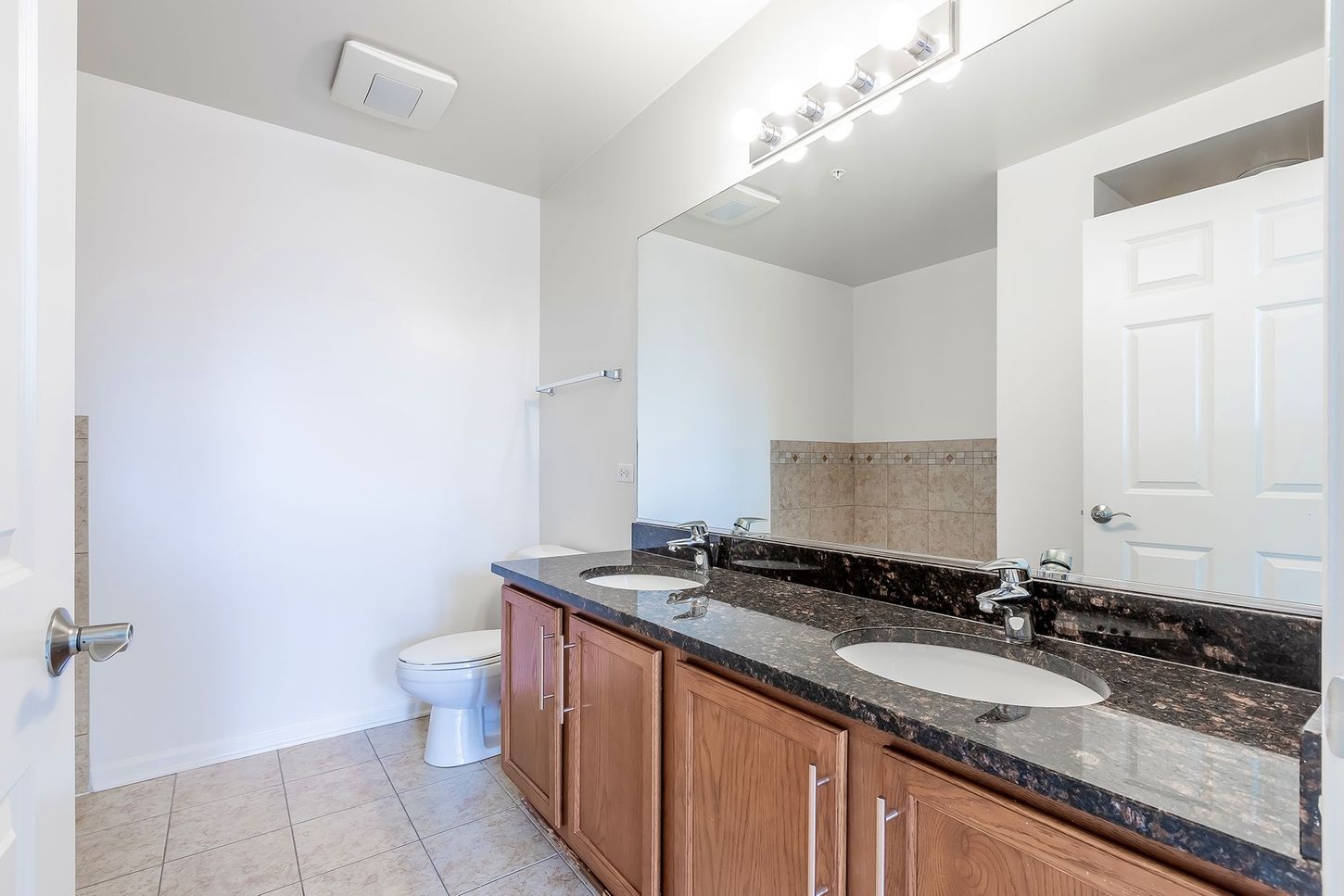 A bathroom with two sinks , a toilet , and a large mirror.