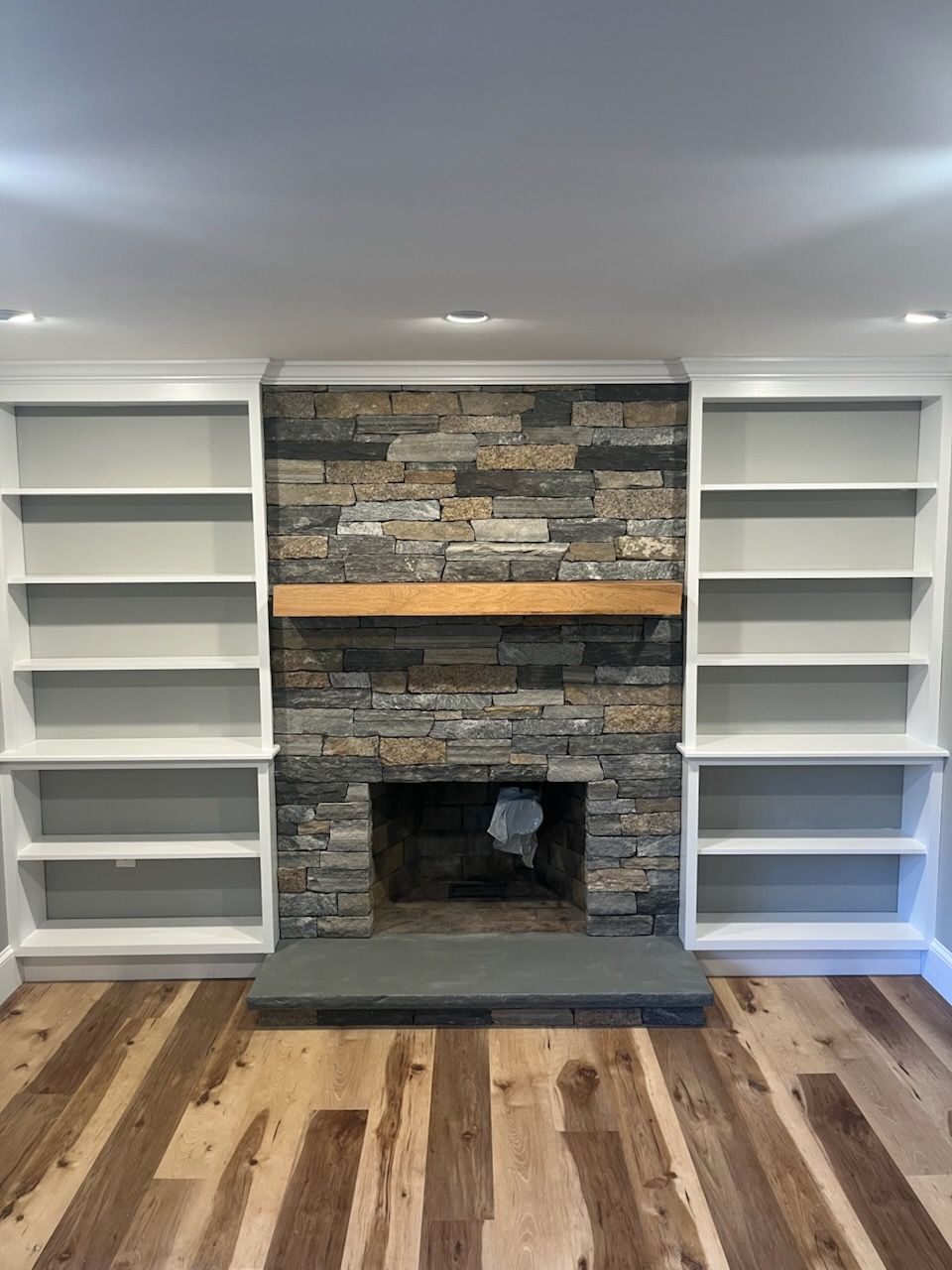 Fireplace with stone surround, wood mantle, and white built-in bookshelves.