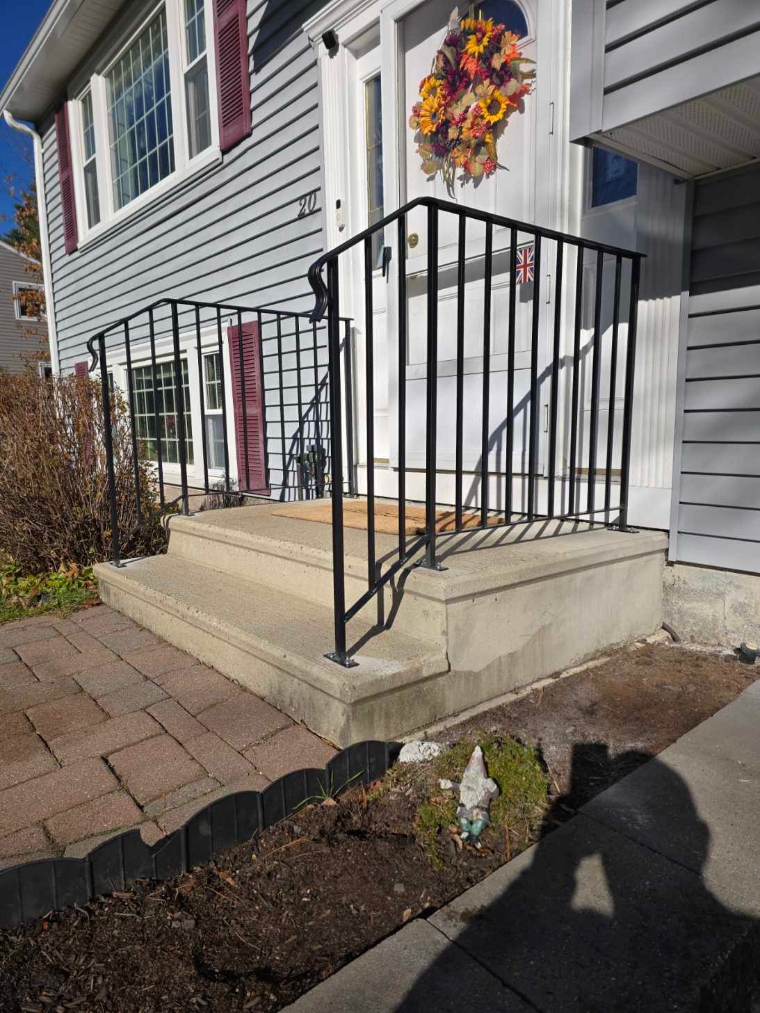 Black metal handrails on concrete steps leading to a house entrance with a wreath.