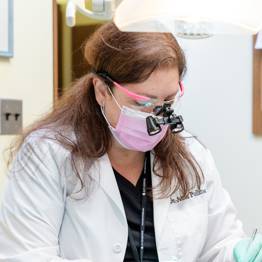 Dentist wearing pink mask and glasses, working in an office with bright lighting.