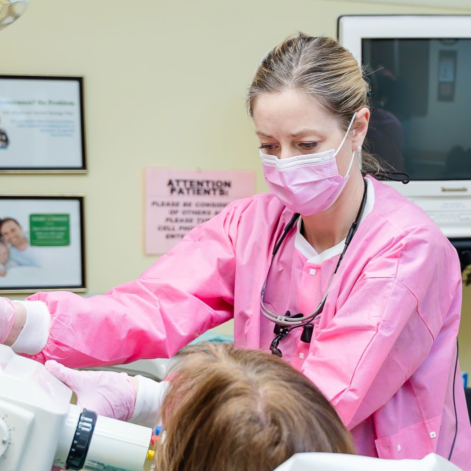 Dentist in pink scrubs and mask takes dental X-ray of a patient in a dental office.