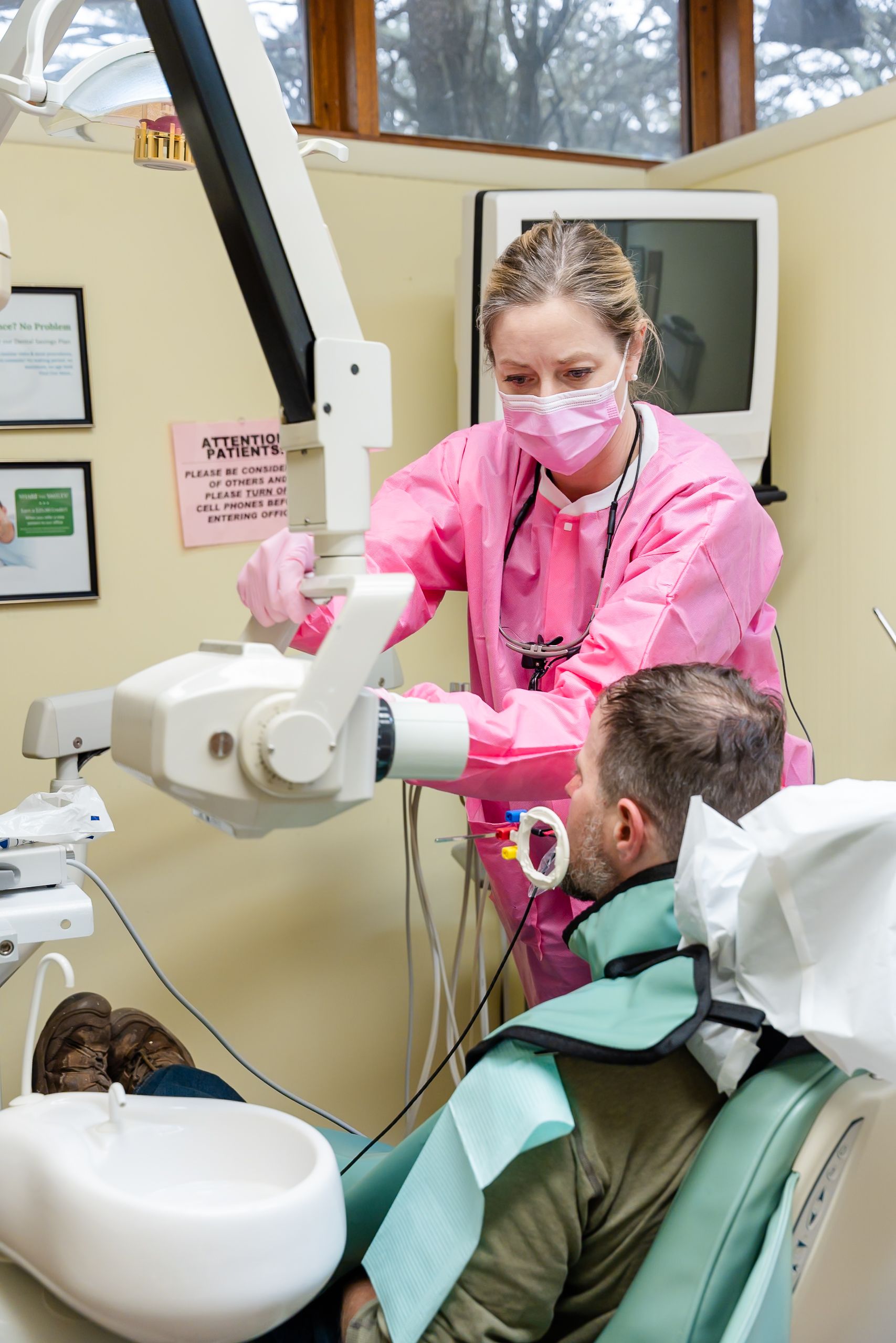 Dental hygienist in pink scrubs taking an X-ray of a patient in a dentist's chair.