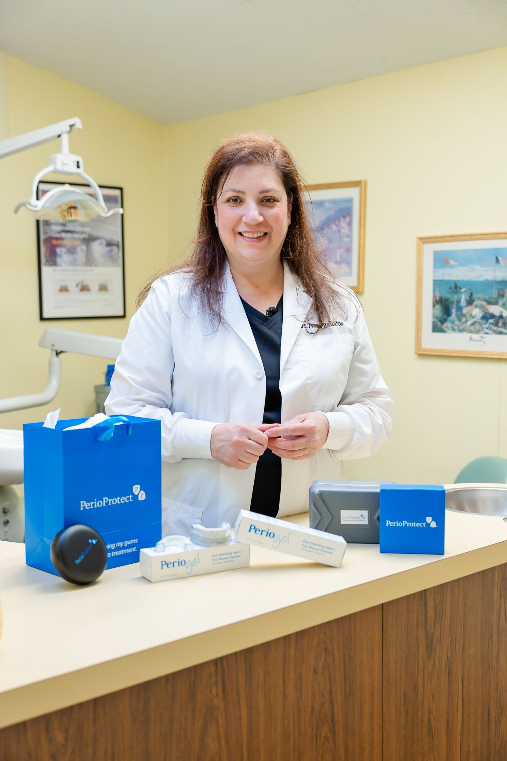 Woman in white lab coat stands behind a dental counter, holding products.
